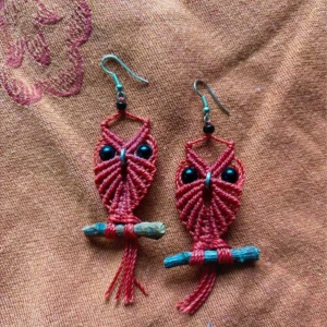 Rosa makramé örhängen med ugglor - Unika handgjorda örhängen i makramé med uggleform, knutna i rosa tråd och dekorerade med svarta pärlor som ögon. Ugglorna sitter på små blå pinnar vilket ger en cool boho-vibe. Perfekt för dig som gillar färgglada och kreativa accessoarer.