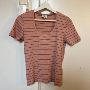 Randig rosa t-shirt från Noa Noa - Rosa ribbad t-shirt från Noa Noa i storlek S. T-shirten har grå tunna ränder, rund halsringning och är kortärmad. 