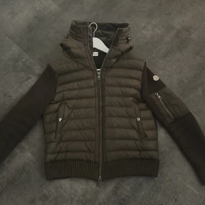 Grön Cardigan från Moncler - Säljer nu min gröna Cardigan från Moncler med stickade ärmar och ribbade muddar. Jackan har huva, dragkedja framtill och två fickor med knappar. Perfekt för höst och vår, riktigt snygg och skön att bära (Medium). Priset är inte hugget i sten och går att förhandla🤝
