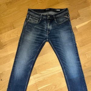 Blå Replay jeans Rocco slim fit - Snygga blå jeans från Replay, modell Rocco, med slim fit passform. Jeansen har klassisk femficksdesign, tydliga slitningar och ljusare partier framtill och baktill. W29/L30