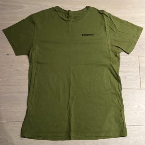 Olivgrön Patagonia t-shirt slim fit - Säljer en olivgrön t-shirt från Patagonia i slim fit med klassisk logga på bröstet och stort tryck på ryggen. Tillverkad i 100% ekologisk bomull, perfekt för dig som gillar stilren och bekväm streetwear.