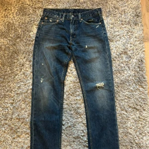 Levi's 501 blå jeans med slitningar - Klassiska Levi's 501 jeans i mörkblå denim med snygga slitningar och distressed detaljer på benen. Står storlek 31/32 men tämligen liten i storlek. 