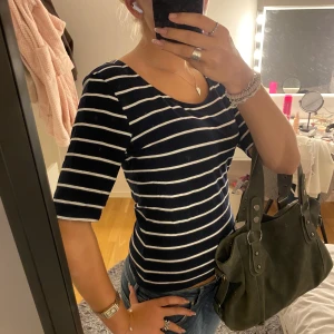 Marinblå randig topp med trekvartsärm - Snygg marinblå topp med vita horisontella ränder och rund halsringning. Modellen har trekvartsärm och sitter slim på kroppen. Perfekt att styla med jeans för en chill look. Materialet känns som mjuk bomull och toppen har en klassisk vibe.