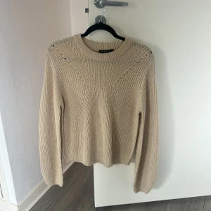 Beige stickad tröja med mönster - Säljer en beige stickad tröja med snyggt stickat mönster upptill. Tröjan har rund halsringning och långa ärmar, perfekt för kyliga dagar. Enkel att matcha med jeans eller kjol.