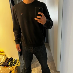 Svart sweatshirt från Champion - Svart crewneck sweatshirt från Champion med liten broderad logga på bröstet. Klassisk modell med rund halsringning och ribbade muddar vid ärmslut och nederkant. Perfekt basic-tröja för en clean och enkel stil. Xl men passar L