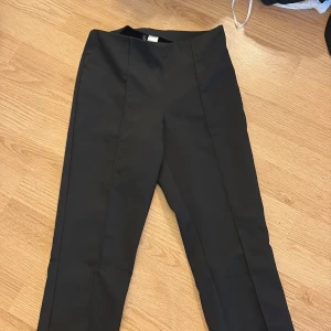 Svarta kostymbyxor från Divided - Snygga svarta kostymbyxor från Divided i storlek 32. Byxorna har en klassisk rak passform med pressveck framtill och midja utan synliga detaljer. Perfekta för en clean och stilren look.