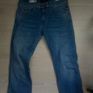 Replay Anbass slim fit jeans blå - Säljer ett par Replay Anbass slim fit jeans i klassisk blå tvätt. Jeansen har fem fickor, dragkedjegylf och snygga slitningar framtill. Perfekt passform med smalare ben och bekvämt material i bomull med stretch.