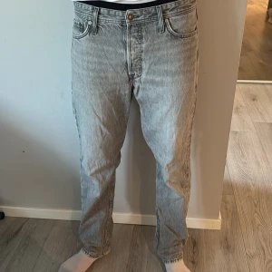 Grå jeans från Jack & Jones - Säljer ett par grå jeans från Jack & Jones med klassisk femficksdesign och snyggt tvättad look. Jeansen har rak passform, normal midja och är tillverkade i bomull. Perfekta för dig som gillar en avslappnad stil. Waist:31 Längd:32