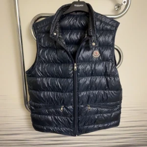 Moncler Gui size 4 - Säljer Moncler Gui dunväst i mörkblå Navy storlek 4 (L/XL) som passar ca 180–190 cm, normal eller slim build. Klassisk och stilren modell perfekt för lager på lager året runt.  100% äkta med alla etiketter, loggor och Certilogo kvar. Digitalt kvitto medföljer. Moncler patch på bröstet, dragkedja med logga, två framfickor och premium dunfyllning Classe 1.  Skick 8–9/10, inga hål eller fläckar, endast mindre spår av användning.  Nypris ca 7000–8000 kr, mitt pris 3500kr 