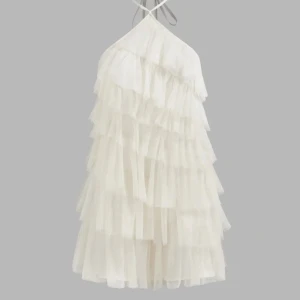 Vit volang klänning  - Supersöt vit kortklänning med glittrigt tyg och flera lager volanger. Halterneck med smala band som korsas fram och öppen rygg. Perfekt för dig som vill sticka ut med en unik och festlig look. Klänningen har en lätt och fluffig känsla som ger extra wow-effekt. Aldrig använd. 