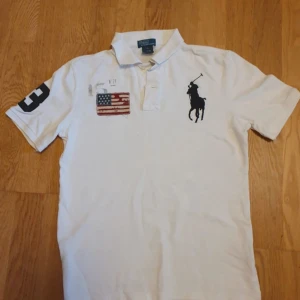 Vit Polo Ralph Lauren t-shirt S - Vit t-shirt från Polo Ralph Lauren med klassisk polokrage och korta ärmar. Stor svart polospelare broderad på bröstet och amerikansk flagga patch. Siffra 3 på ena ärmen. Tillverkad i 100% bomull, loose fit och riktigt clean stil.