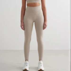 Beige ribbade leggings Aim'n - Snygga beige ribbade leggings från Aim'n med hög midja och tight passform. De är tillverkade i ett stretchigt material som sitter skönt och formar sig efter kroppen. Perfekta för träning eller chill dagar. Diskret logga på höften och stilren look.