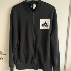 Adidas ziptröja - Strl L - Svart Adidas ziptröja i storlek L. Tröjan är i mycket gott skick och har en klassisk design med hel dragkedja framtill. Passar både till vardagsbruk och träning.