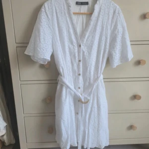 Vit broderad kortklänning från Zara - Vit  broderad kortklänning från ZaraSuperfin vit kortklänning från Zara med broderade detaljer, v-ringning och knappar framtill. Klänningen har korta ärmar och ett bälte i midjan med guldfärgad ring. Perfekt för sommarens alla tillfällen!