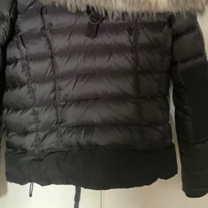 Svart dunjacka med päls från Rockandblue - Snygg svart dunjacka från Rockandblue med fluffig päls runt huvan. Jackan har quiltad design, dragkedja framtill och praktiska fickor med dragkedja.  Säljs pågrund av att den är för liten 