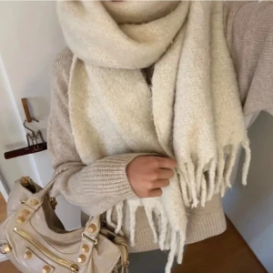 Beige stickad halsduk med fransar - Supermjuk och stor beige stickad halsduk med långa fransar i ändarna. Perfekt att vira flera varv runt halsen för en mysig look. Passar dig som gillar neutrala toner och vill ha en varm accessoar till vintern.