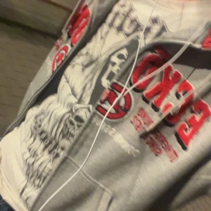 Grå hoodie från Ecko Unltd med röd text - Säljer en grå hoodie från Ecko Unltd med stora röda och vita tryck på bröstet och ärmen. Tröjan har huva med röd insida, känguruficka och ribbade muddar. Perfekt för dig som gillar streetwear och vill sticka ut med en klassisk look.