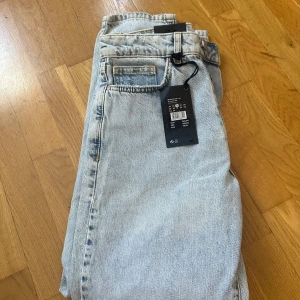 Never Denim ljusa raka jeans - Säljer ett par ljusblå jeans från Never Denim med rak passform och hög midja. Jeansen har klassisk femficksdesign, raka ben och är tillverkade i bomull. Perfekta för dig som gillar en clean och avslappnad look.