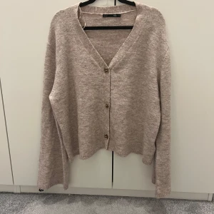 Beige oversized kofta med knappar - Supermjuk beige kofta från H&M med v-ringning och stora knappar framtill. Koftan har en oversized passform och långa ärmar med lätt ribbade muddar. Perfekt för lager-på-lager och chill dagar.