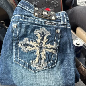 Vintage Miss Me jeans bootcut - Snygga blå jeans från Miss Me med bootcut, med en stor broderad korsdetalj på bakfickan och dekorativa nitar. Jeansen har kontrastsömmar, klassisk femficksdesign och är tillverkade i bomull med lite stretch för skön passform. Storlek 30/34. Pris kan diskuteras