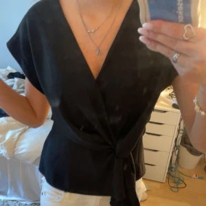 Svart omlottopp  - Super snygg svart omlottopp från Zara med v-ringning och knyt i midjan. Perfekt till fest men även skolan. Super fint att matcha med jeans eller kjol. Säljs pgv att den inte tyvärr inte används. 