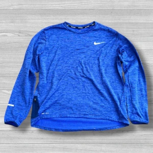 Nike running - Nike Dri-Fit långärmad tröja i blått med diskret mönster och vit logga på bröstet. Tröjan är tillverkad i ett tekniskt, syntetiskt material som andas och passar perfekt för träning. Rund halsringning och sportig look.