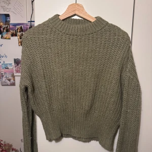 Olivgrön stickad tröja med ribbad kant - Säljer en olivgrön stickad tröja med grov struktur och ribbad kant vid hals. Croppad, snygg med vitt linne ute och lowwaist jeans