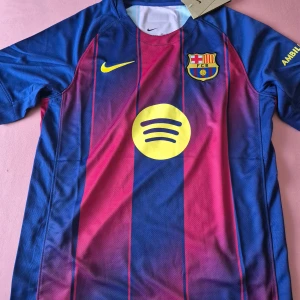 FC Barcelona matchtröja Nike - Snygg FC Barcelona matchtröja från Nike med klassiska blå och vinröda ränder, gult Spotify-tryck på bröstet och klubbmärke. Kortärmad modell i lätt, ventilerande polyester. Ambilight tv-tryck på ärmen och UNHCR-logga på ryggen. Perfekt för dig som älskar Barca!