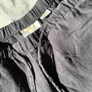 Svarta linnebyxor från Gina Tricot - Svarta linnebyxor från Gina Tricot med avslappnad passform och resår i midjan. Byxorna har dragsko och raka ben, vilket gör dem riktigt sköna och lätta att bära. Perfekta för en chill och stilren look.