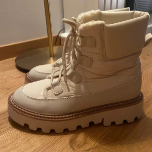 Chunky vita vinterboots med snörning - Snygga chunky boots i vitt med grov sula och snörning framtill. Fodrade med mjukt fuskpälsfoder för extra värme. Perfekta för kalla dagar och ger en cool look till vinteroutfiten.