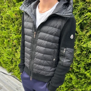 Svart Moncler cardigan - Säljer en svart cardigan från Moncler med stickade ärmar och huva. Jackan har dragkedja framtill, quiltad framsida och en ficka med dragkedja på ärmen. Perfekt för dig som vill ha en snygg look. Tveka inte vid frågor osv. 
