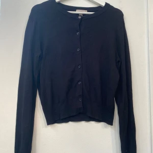 Svart kofta från H&M, storlek M - En klassisk svart kofta från H&M i storlek M. Koftan har rund halsringning, långa ärmar och knäppning med svarta knappar framtill. 