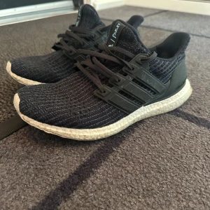 Adidas Ultraboost Parley sneakers - Adidas Ultraboost Parley sneakers med stickad ovandel och vita Boost-sulor. Skorna har klassiska tre ränder på sidan, snörning och detaljer i syntet. Perfekta för dig som gillar stilrena och bekväma sneakers med modern känsla.
