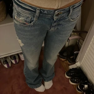 Diesel bootcut jeans i ljusblå denim - Bootcut jeans från Diesel i ljusblå tvättad denim med slitna detaljer på låret och klassiska fem fickor. Jeansen har låg midja. Perfekta för en avslappnad och trendig look. Midjemått: 78 cm | W27, står inte längd men har ett par diesel jeans i W30 och dessa är några cm längre så L32 skulle jag tro! Nypris ligger på 2500