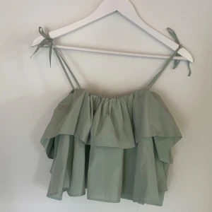 Grön volangig linnetopp från Zara - Superfin ljusgrön linnetopp från Zara med volanger och smala axelband som knyts upptill. Toppen är luftig och har en flowy passform, perfekt för varma dagar. Snygg att styla med jeans eller kjol för en trendig look. 