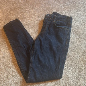 Mörkblå jeans från John Henric W31 - Snygga mörkblå jeans från John Henric med klassisk femficksdesign och kontrastsömmar. Jeansen är tillverkade av 79% bomull, 20% återvunnen polyester och 1% lycra för en bekväm passform. Perfekta till vardags med stilren look och läderpatch bak.