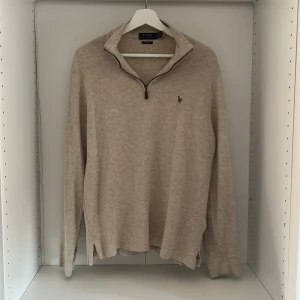 Beige half zip tröja från Polo Ralph Lauren - Snygg beige långärmad tröja från Polo Ralph Lauren med half zip och klassisk broderad logga på bröstet. Tröjan är i mjuk bomull och har en avslappnad passform, perfekt för lager-på-lager under hösten och våren. Lite stora i armarna.