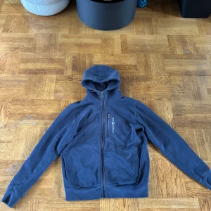 Mörkblå hoodie från Sail Racing - Mörkblå hoodie från Sail Racing med dragkedja hela vägen. Använd ett fåtal gånger för jag inte gillar den längre. Liten mörk fläck längs fram på armen men den ser man knappt.