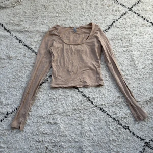 Beige långärmad topp från H&M Divided - En enkel och stilren beige långärmad topp från H&M Divided. Modellen är croppad med rundad urringning och smal passform. Perfekt att matcha med jeans eller kjol för en clean look. Tillverkad i mjuk bomull som känns skön mot huden.