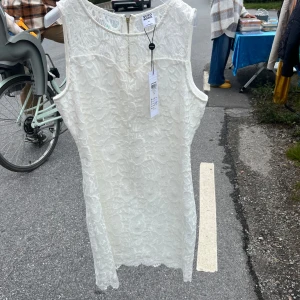 Vit spetsklänning från Vero Moda - HELT NY! GANSKA LITEN I STORLEK SKULLE SÄGA TYP EN S!! ALDRIG ANDVÄND PRISLAPP FINS SOM SAGT.                        .    Supersnygg vit kortklänning från Vero Moda i storlek 40. Klänningen är ärmlös och har ett vackert blommigt spetsmönster över hela plagget. Den har en rak passform och en lång dragkedja i ryggen som gör den enkel att ta på. Perfekt för dig som gillar stilrena detaljer!