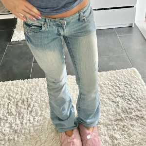 Ljusblå bootcut jeans med slitningar - Säljer ett par ljusblå bootcut jeans med snygga slitningar på benen och broderade detaljer på bakfickorna. Jeansen har låg midja och klassisk femficksmodell. Perfekta för dig som gillar en avslappnad och trendig look.