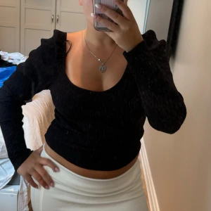 Svart ribbad topp med puffärm  - Svart ribbad topp från H&M med långa puffärmar och djup, fyrkantig urringning. Toppen är croppad och har en figurnära passform som framhäver siluetten. Perfekt för dig som gillar trendiga detaljer och stilren look.