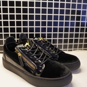 Svarta sneakers från Giuseppe Zanotti - Snygga svarta sneakers från Giuseppe Zanotti med lyxiga gulddetaljer, dragkedjor på sidorna och snörning. Skorna har en mix av sammet och lackdetaljer som ger en exklusiv känsla. Perfekta för dig som vill sticka ut med stilrena och trendiga skor.