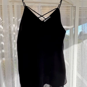 Svart linnetopp från Pieces - Säljer en svart linnetopp från Pieces i storlek M. Toppen har tunna axelband och snygga korsade band framtill som ger en extra detalj. Materialet är lätt och luftigt, perfekt för varma dagar eller lager på lager. Enkel och stilren design som passar till mycket.