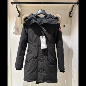 Canada Goose Svart Rossclair Parka jacka  - Säljer en svart Canada Goose Rossclair Parka i storlek XS, passar även i S. Jackan har en dragkedja och knappar framtill, samt fem olika fickor. Fri frakt på denna.