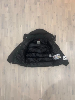 Svart dunjacka från Moncler - Säljer en svart dunjacka från Moncler med klassisk quiltad design och ficka med Moncler-logga på ärmen. Jackan har lång ärm, dragkedja och tryckknappar. Perfekt för kalla dagar och riktigt snygg till streetwear-stilen.