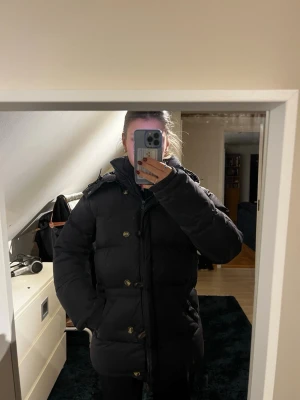 Mörkblå lång dunjacka med huva - Snygg mörkblå dunjacka med huva och knappar framtill från Bommerang i storlek xs. Jackan är lång, har en pufferstil och stora fickor på sidorna. Perfekt för kalla dagar och har en klassisk look som passar till det mesta. Hade ett litet hål vid ärmen som är ihop sytt. Inga andra defekter bortsett från de. Nypris: 7000kr.🤗🤗