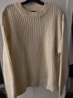 Krämvit stickad tröja från Lager 157 - Säljer en krämvit stickad tröja från Lager 157 med grovstickad struktur och rund hals. Tröjan har långa ärmar och bred ribbstickad mudd vid ärmslut och nederkant. Perfekt för lager på lager under kyliga dagar.