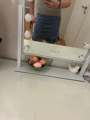 Blå blommig kortkjol med snörning - Supersöt blå kortkjol med vitt blommönster och snörningsdetalj framtill. Kjolen har en avslappnad passform och är perfekt för varma dagar. Tyget känns lätt och flowy, vilket gör den skön att bära.