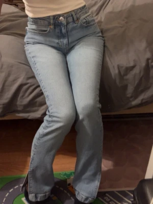 Ljusblåa slim split jeans - Säljer ett par ljusblåa slim split jeans från Bikbok med slit och hög midja. Klassisk femficksmodell med bälteshällor och snyggt läderpatch bak. Perfekta till en avslappnad och trendig look. Passar även xs! 